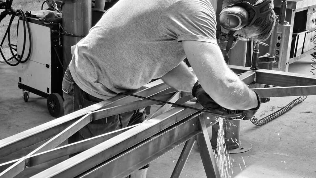 Maxime travaillant à la meuleuse sur une structure en acier destinée à une pergola métallique sur mesure.