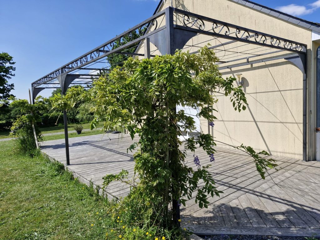 Pergola métallique végétalisée avec glycine et volutes en acier