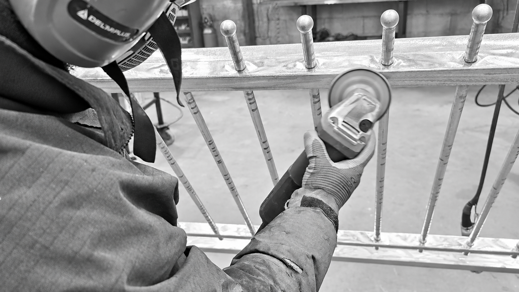 Maxime effectuant le ponçage de la galvanisation d'un portail en acier sur mesure avant thermolaquage.