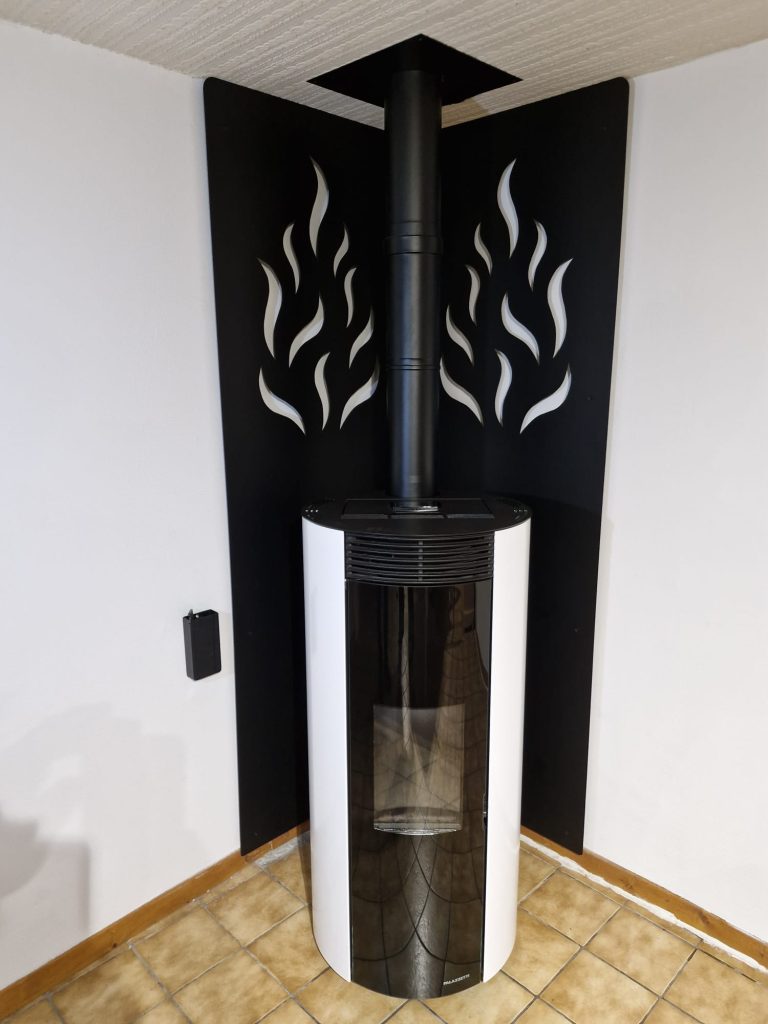 Tôle décorative en acier thermolaqué noir avec motifs flammes derrière un poêle à granulés